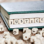 Image of a book with little wooden blocks that spell the word justice in between the pages