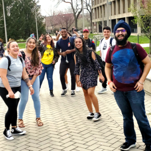 A group of students smile for a picture near campus buildings