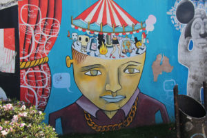 A mural of a sad-looking boy who has a carousel coming out of the top of his head - but the carousel is made op of strange creatures and symbols. 