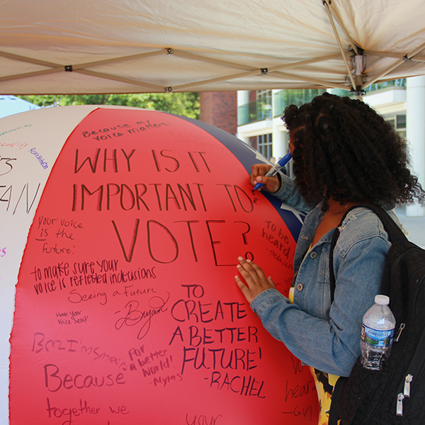 A student signs a giant beach ball with messages about active voting