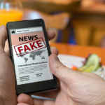 Person holding a cell phone that reads "Fake News"