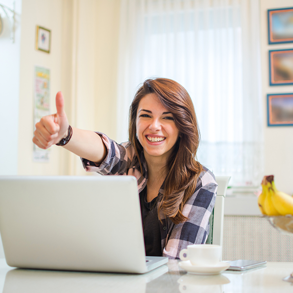 A young woman at a laptop giving thumbs up to the camera