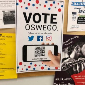 Bulletin board with a poster in the center with the words “Vote Oswego. Follow us on social media; Twitter, Facebook, and Instagram logos; and, a hand holding a smart phone displaying a QR code and voteoswego.com