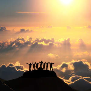 A group of people celebrate atop a mountain, looking at sunbeams shoot through the clouds